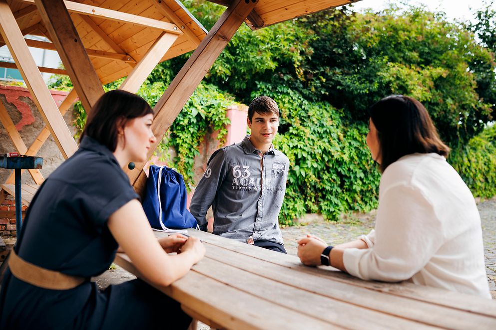 Zwei Frauen und ein junger Mann sitzen an einem Tisch und unterhalten sich